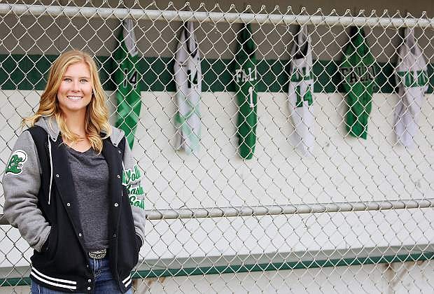 Megan McCormick stands afront her home dugout while jerseys from each sport she&#039;s played, including softball, volleyball and basketball, hang in the background.