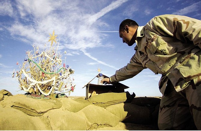 Gunnery Sgt. Aniceto Hernandez, from Bakersfield, Calif., adjusts an angel made of a water bottle on the Nativity scene he constructed from a ration box at the edge of his fox hole on Camp Rhino, Afghanistan, Saturday, Dec. 15, 2001.  Hernandez and his Marines also made a Christmas tree from a local bush, left, and decorated it Marine-style: shotgun shells, bullets and water bottle caps. (AP Photo/Earnie Grafton, Pool)