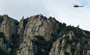 A helicopter circles over the mountain where a Navy helicopter, white wreckage at left center, crashed near  Lake Isabella, Calif. on Thursday, March 28, 2002. Two people were killed and four others were injured in the crash.(AP Photo/Bakersfield Californian, Felix Adamo)