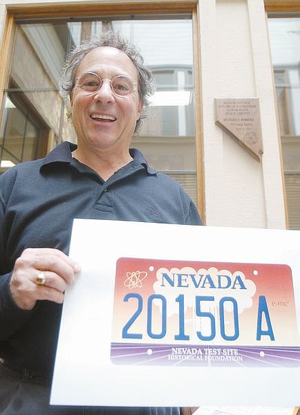 Richard Bibbero stands in his office in Gardernerville with a copy of a new Nevada Licence Plate for the Nevada Test Site Historical Foundation that he disigned and sketched. His design was chosen when he submitted it in a contest. Photo by Brian Corley