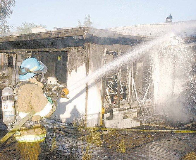 Photo by Brian CorleyCarson City Firefighter Tim Dehaven puts water on a portion of the back of a house that burned early Monday morning. The fire spread through the house an damaged the house next door.