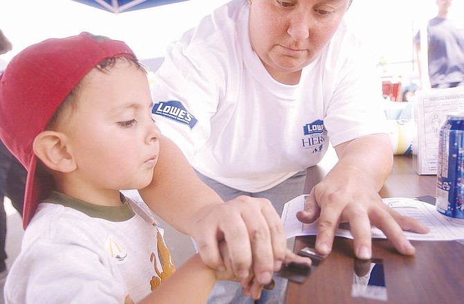 Johnathan Lessard, 4, left, watches as his mother, Denise Lessard, puts ink on his fingers while he has his finger prints recorded at Lowes Saturday during a Safety Day for Kids.Hundreds of parents had their childrens&#039; finger prints recorded to help track them in the event of an abduction. Photo by Brian Corley