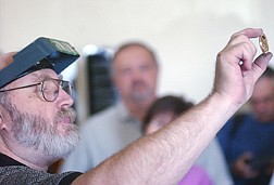 Ken Hopple, a coin press operator, holds up a coin to onlookers at the Nevada State Museum Friday. The press at the Museum was in operation minting coins for the 100th anniversary of the Gold Field Mining Camp. Photo by Brian Corley