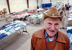 Chas Fisher stands in front of several row of tables stacked with material that his wife, who now suffers from Alzhiemer&#039;s disease, was going to use for quilt material. The fabrics will be sold by the 4-H which Fisher has been a volunteer for more than 50 years. Photo by Brian Corley