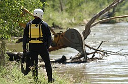A Search and Rescue team member watches the waterTuesday morning while a backhoe clears a dense debris field from the Carson River location where a Dayton man went missing.   photo by Rick Gunn
