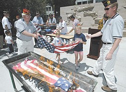 American Legion member Ron Gutzman, left, helps his granddaughters Deelany Grant, 6, and Jazmin Grant, 9, place a retired flag into the fire during the annual Boys State flag retirement ceremony on Thursday.  Tim Tetz, the director of Boys State, right, says each flag is retired in ceremony because each has meaning.