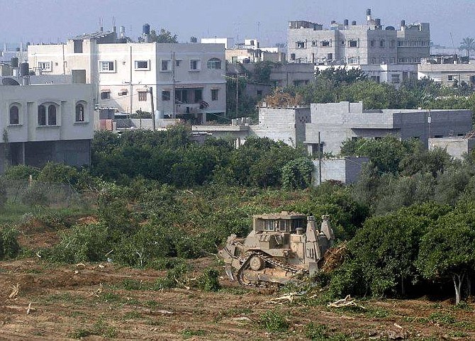 An Israeli army bulldozer uproots orange trees in the outskirts of the northern Gaza town of Beit Hanoun, background, as fighting goes on in the city during a major Israeli army incursion Thursday July 8, 2004.  Israeli troops and Palestinian gunmen fought fiercely in Beit Hanoun Thursday. At least six Palestinians, among them three militants and a 35-year-old woman, have been killed, Palestinians and the Israeli army said. (AP Photo/Hatem Moussa)