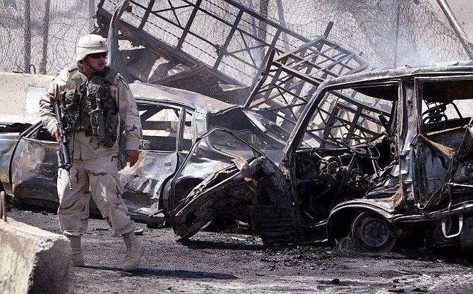 An American soldier secures the scene of a car bomb explosion in Baghdad, Iraq July 14, 2004. The car bomb exploded at a checkpoint near an area housing international offices and embassies killing at least 10 people and injuring 40. (AP Photo/Joe Raedle/Pool)