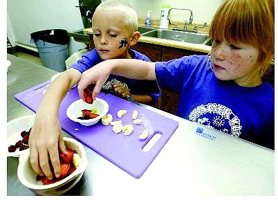 Belinda Grant/Nevada Appeal Joseph Glahn and Mackenzie Gilliam, both 6 years old, reach for berries to make fake soup. They are attending a cooking class with Kick Back Camp in Mills park gymnasium kitchen. The classes will go through the summer every Monday.