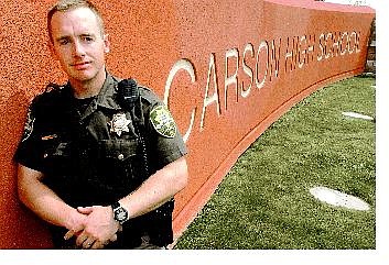 Rick Gunn/Nevada Appeal New Carson City School cop and Carson City deputy Dean Williams stands next to the Carson City High School sign Friday.
