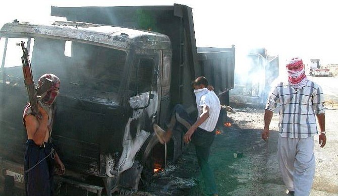Insurgents stand near military supply convoy trucks destroyed by them at Hit, 110 kilometers (68 miles) west of Baghdad, Tuesday, Aug. 31, 2004, in this photograph made available on Sept 1. Four trucks could be seen smoldering on the highway after the attack and four Iraqi drivers working for foreign contractors were allegedly kidnapped. (AP Photo/Ali Ahmed)