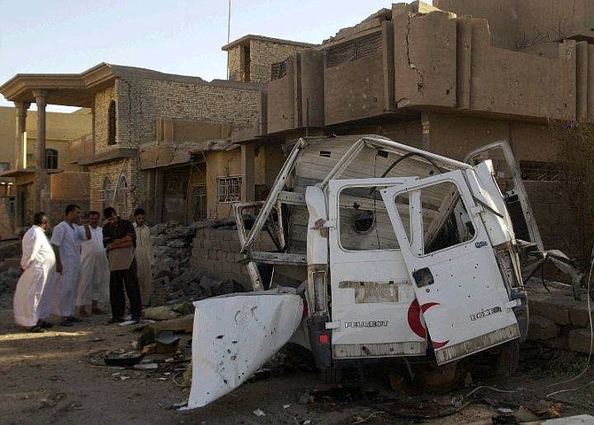 Local residents look at a destroyed ambulance belonging to the Iraqi Red Crescent, after U.S. warplanes and artillery bombed the Sunni insurgent stronghold of Fallujah, Iraq,  Monday Sept. 13, 2004. The ambulance, which was rushing from the area of the blasts was hit by a shell, killing the driver, a paramedic and five patients inside the vehicle, said  Fallujah General Hospital official, Hamid Salaman. The U.S. military said the bombings were part of a precision strike on a site where several members of an al-Qaida-linked group led by Jordanian-born terror suspect Abu Musab al-Zarqawi were meeting, At least 20 people were killed, including women and children, and 29 others wounded, in the bombing, according to another hospital official. (AP Photo/Bilal Hussein)