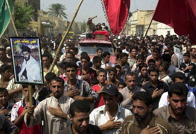 A man displays a portrait of Shiite cleric Muqtada al-Sadr, left,  as mourners join a procession for the burial of Majid Hameed, at Sadr City, Baghdad, Iraq, Friday Sept. 24, 2004. Hameed was killed in an airstrike early Friday morning. (AP Photo/Karim Kadim)