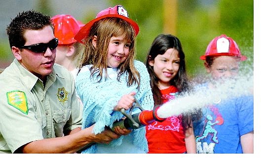 Christi Donaldson, 6, knocks a bucket off a table about 10 feet away at Fritsch Elementary School with the assistance of Nevada Division of Forestry firefighter Micah Horton at the Carson City school on Friday morning. Below, Fritsch students watch to see how far Horton can spray water from the hose at the school Friday.   BRAD HORN/Nevada Appeal