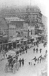 Main Street, C Street, Virginia City, during what looks like a Fourth of July Parade. The International Hotel looms in the background. The first International was a joint venture by Isaac Bateman and Andrew Paul and was a single story built of rough-hewn timbers cut from Six Mile Canyon.
