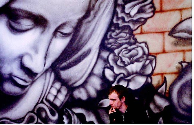 Rick Gunn/Nevada Appeal Carson City artist Jamie Thornley sits next to his mural of the Virgin Mary at Java Joe&#039;s on Thursday. Thornley will complete murals on the ceiling and eventually cover all the walls with his artwork.