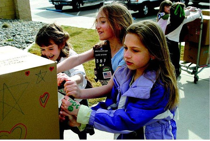 Emma Garrard/Nevada Appeal Girl Scouts Katie Matuska, 6, Natalie Williams, 7, and Kylie Couste, 8, push a box of Girl Scout Cookies into the Post Office on Roop Street on Thursday. The Girl Scouts are sending 489 boxes of cookies to U.S. troops in Iraq.