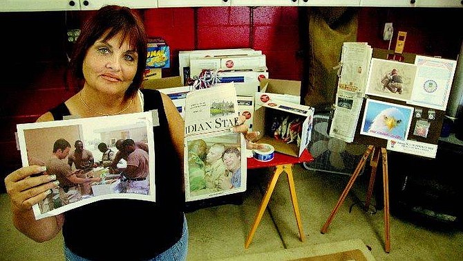 Kevin Clifford/Nevada Appeal P.J. Degross of Carson City stands in front of her Web of Support work station Thursday in her garage where she ships goods to deployed soldiers of the Mississippi National Guard. She holds a picture of soldiers receiving the packages she sent and a newspaper article about Sgt. Norris Galatas, who asked her to help his men after being injured.