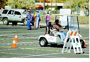 BRAD HORN/Nevada Appeal Katie Carlevato, 14, drives a golf cart through an obstacle course wearing drunk goggles, while her friend Amanda Wong, 13, enjoys the ride during the Community Awareness Fair at Carson High School on Saturday. The vehicle in back shows what happens when people drive while impaired by alcohol.
