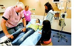 Cathleen Allison/Nevada Appeal Dr. Richard Newbold, an emergency room physician, and registered nurse Barbara Lehn check out Katharyn Woods, 10, as her mom. Mary. and sister Emily look on Wednesday during an operations simulation at the new Carson Tahoe Regional Medical Center. Woods was pretending to have a head injury from a fall off a horse as part of the drill.