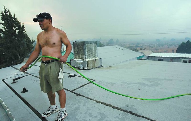 Chad Lundquist/Nevada AppealJon Jon Aragon hoses off the roof of his Pyrite Drive home Monday while flames, obscured by thick, gray smoke, approached the Mound House neighborhood. Hundreds of homes are threatened in the 5,000-acre blaze.