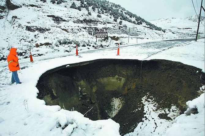 Chad Lundquist/Nevada Appeal A Nevada Department of Transportation employee stands next to a 30-foot-diameter by 25-foot-deep sinkhole on Highway 342 north of Silver City. NDOT expects to have it  repaired by Friday.
