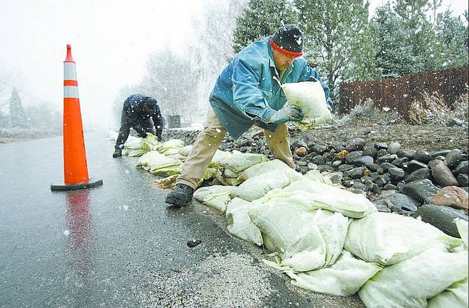 Cathleen Allison/Nevada Appeal Gilbert Estrada, front, and Scott Chaney move sandbags Tuesday morning on Ash Canyon Road near North Winnie Lane. They had placed the bags Monday, but were asked to move them off the street to make way for snowplow access.