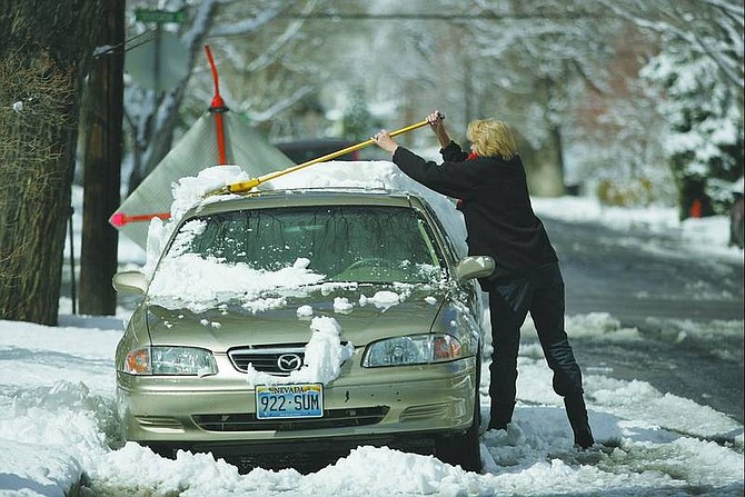 BRAD HORN/Nevada Appeal Christine Giusti brushes snow off her car in downtown Carson City on Friday. The National Weather Service has predicted more snow will fall today.