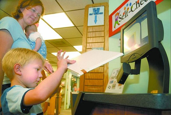 Kevin Clifford/Nevada Appeal Benjamin Sommercorn, 4, checks out a book with the help of his mother, Melissa, using the new self-checkout system Friday morning at the Carson City Library.