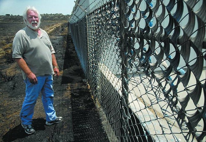 Kevin Clifford/Nevada Appeal Jeff Kyle, owner of Added Storage on Highway 50 East, looks Tuesday at the damage done to his north fence by the Linehan fire Monday night. The plastic on the fence melted by the heat, causing minor property damage.