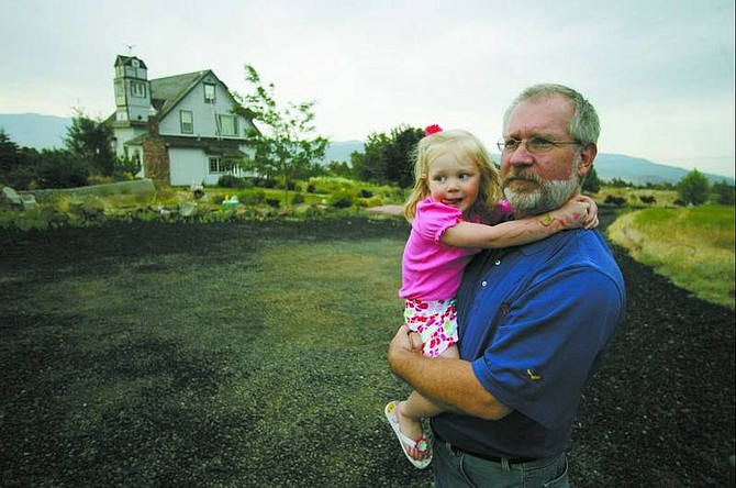 Brad Horn/Nevada Appeal Bob Anderson holds his 3-year-old granddaughter Madison Anderson at their home on Linehan Road in Mound House, after returning Wednesday. Anderson and his family evacuated their property Monday evening after the Linehan Complex fire threatened their Victorian home built in 1876.