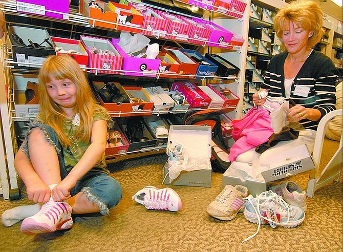 Kevin Clifford/Nevada Appeal Katie, 8, struggles to try on new shoes while Rene Langson, a Kiwanis volunteer, organizes Katie&#039;s pile of clothing and discarded pile of shoes. The two were shopping during the ChildSpree event Saturday morning at Mervyn&#039;s. The event allowed 90 underprivileged children the opportunity to get a $100 worth of new school clothes.