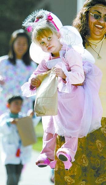 Cathleen Allison/Nevada Appeal Angeles Zarate carries Emily Marschall, 2, at the end of a trick-or-treating trek around the Western Nevada Community College campus Tuesday morning. The staff, children and a number of parents from the WNCC Child Development Center participated in the annual Pumpkin Parade.