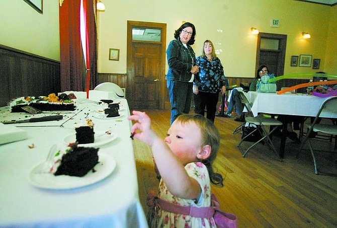 BRAD HORN/Nevada Appeal Emma Cavner, 18-months-old, sneaks a piece of cake while her mother, Polly Cavner, right, and Lorraine Vazquez, of Minden, watch during the National Adoption Day celebration Saturday at the Brewery Arts Center.