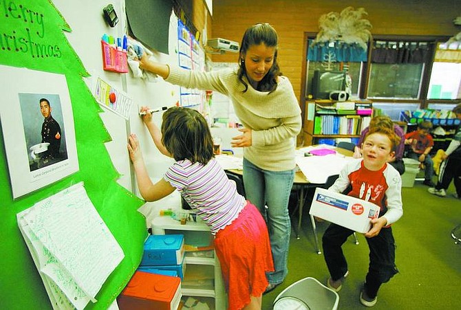 BRAD HORN/Nevada Appeal Melanie Allec, 7, writes the weight of her group&#039;s care package on the board in Robin Kato, center, and Tara Hornemann&#039;s first/second-grade classroom at Seeliger Elementary School on Friday. Derek Barry, 7, right, carries the box that&#039;s ready to ship. The class is sending care packages to troops in Iraq. Kato&#039;s brother Marine Lance Cpl. Bradford H. Kato, pictured in photo to left, was deployed to Iraq in September.
