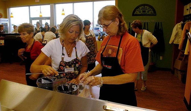Jim Commentucci/The Post-Standard Make and Take Gourmet owner Michele Bellso, center, helps Barbara Fanizzi make lemon Parmesan tilapia at the meal-assembly kitchen in Cicero, N.Y., Aug. 30.