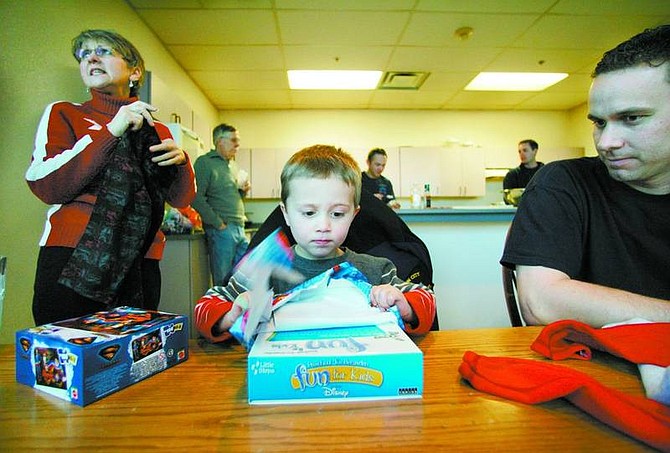 BRAD HORN/Nevada Appeal Carson City firefighter Bryon Hunt watches his 3-year-old son Tyler open a present while Meri Gscheidle, Bryon&#039;s mother, puts away Tyler&#039;s other gifts on Monday afternoon.