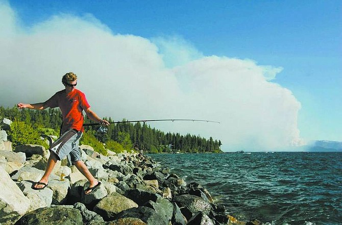 BRAD HORN/Nevada Appeal Dave Sherman, of South Lake Tahoe, fishes near Cave Rock on Sunday afternoon while the Angora fire burns in the background.