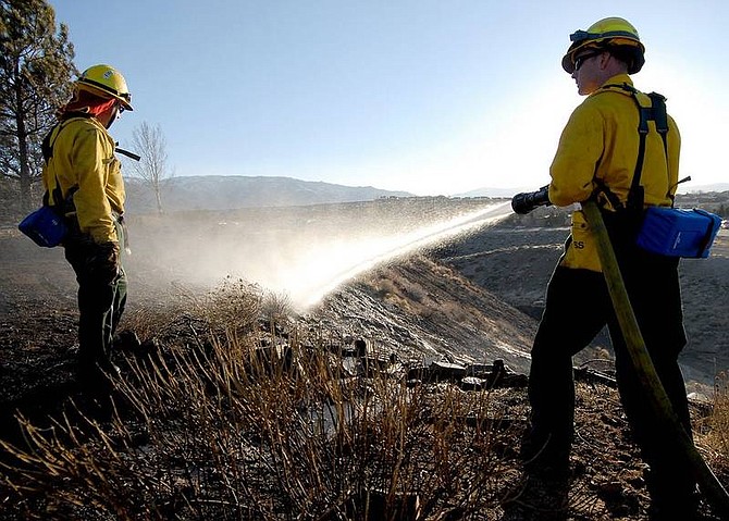 Sparks firefighters Matt Joseph, right, and Mike Foster water down hot spots after a fire behind Heights Drive in Reno, Nev., Saturday, March 17, 2007. (AP Photo/Nevada Appeal, Kevin Clifford)