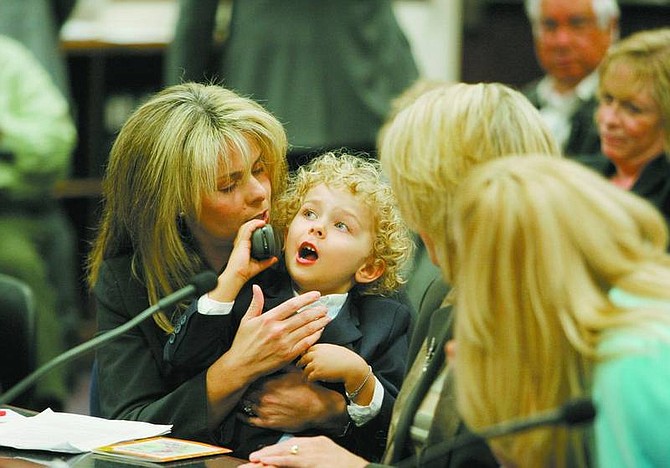 Brad Horn/Nevada Appeal Heather Andrews holds her 3-year-old son Sterling Andrews, of Reno, while he tries to talk on her cell phone during a Senate Commerce and Labor work session at the Nevada State Legislature on Friday. Sterling was born profoundly deaf and received cochlear implants when he was 1-year-old. His mother Heather testified in front of the committee.