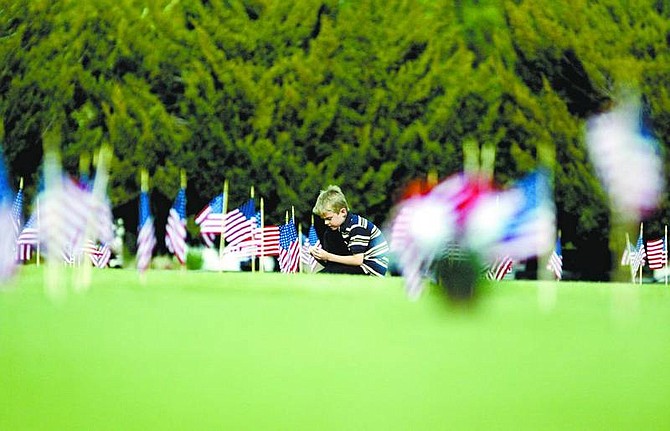 BRAD HORN/Nevada Appeal Jesse Bensinger, 7, of Carson City, helps arrange American flags on gravesites of Veterans at the Lone Mountain Cemetery on Friday afternoon.