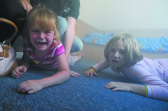 Kevin Clifford/Nevada Appeal Madi McKee, 5, left, of Casron City cries out of fright and is comforted by her mother Kim McKee and Carson City Community Emergency Response Team (CERT) member Charyl Keen while her sister Courtney McKee, 7, crawls on the ground during the smoke demostration inside the Carson City Fire Department All Hazards Safety House at the National Night Out event at Mills Park on Tuesday.