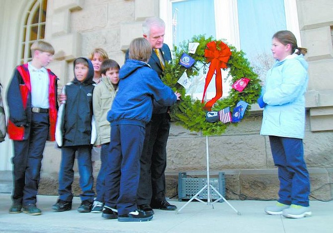 Amy Lisenbe/Nevada Appeal St. Teresa School fourth-graders Jacob Sheldon, center, and Grace Bayliss, right, help Governor Jim Gibbons place a wreath on the Nevada Capitol steps to honor veterans and active military duty on Monday morning as part of the Wreaths Across America Project.