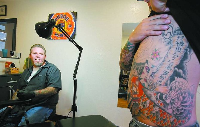 BRAD HORN/Nevada Appeal Robert Klingel displays some of his tattoos created by Hooligans Ink owner Sean Dawley, pictured at left.