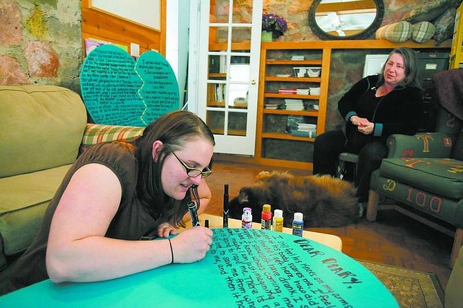Brad Horn/Nevada AppealSarah Andrews writes the story of a woman who was sexually assaulted on a wooden teal heart while &quot;Marsha&quot; sits with her dog Rusty in the background, on Saturday. Marsha, whose name was changed to protect her identity, is the victim of a sexual assault that occurred 40 years ago.