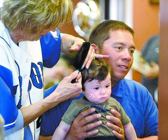 Amy Lisenbe/Nevada Appeal Brandy Plattsmier, left, owner of Attitudes Salon, gives six-month-old Ethan Cook, son of coach Steve Cook, right, his first haircut during a haircut-a-thon at her business to benefit the Carson High School baseball program Sunday afternoon.