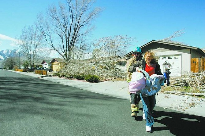 BRAD HORN/Nevada AppealCarson City firefighter Jim White escorts Desiree Mefford, Trinity Mefford, 4 months, and Gage Becker, 13, along with the family&#039;s dog Roco, from their Hampton Drive home after a 40-foot-tall cottonwood fell onto their home on Wednesday afternoon.