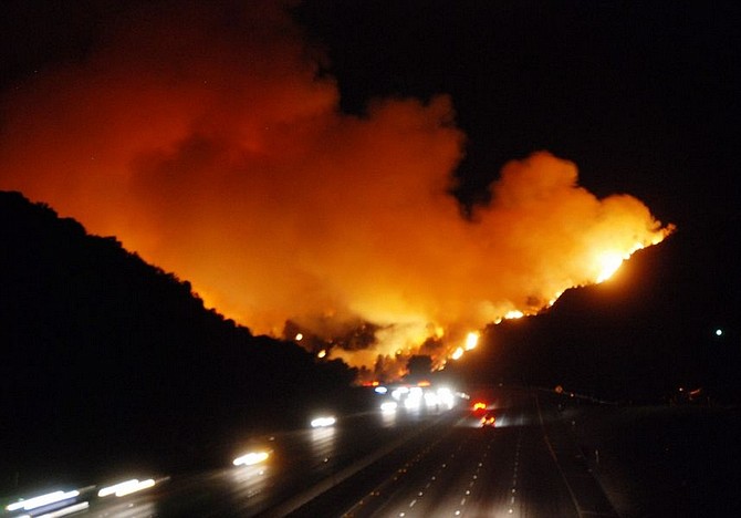 Flames and smoke from a wildfire fire burning in the Sepulveda Pass area of Los Angeles near Brentwood light up the sky as traffic moves ahead on the freeway. Authorities say the wildfire is burning at least 150 acres in west Los Angeles near the Getty Center museum and a portion of the San Diego Freeway has been shut down. (AP Photo/Mike Meadows)