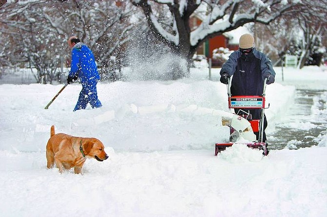 Amy Lisenbe/Nevada Appeal Michael Kubel, 16, right, helps his father, Steve, remove snow from the walk and sidewalks surrounding his office in Carson City Sunday morning as their yellow lab Autumn plays in the snow banks.