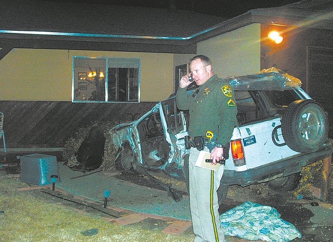 F.T. Norton/Nevada AppealDeputy Nathan Brehm stands next to a badly damaged GMC Jimmy against the garage at 2104 Darla Way. Two men were critically injured after the Jimmy struck a tree, ejecting the driver, before crashing into the garage.